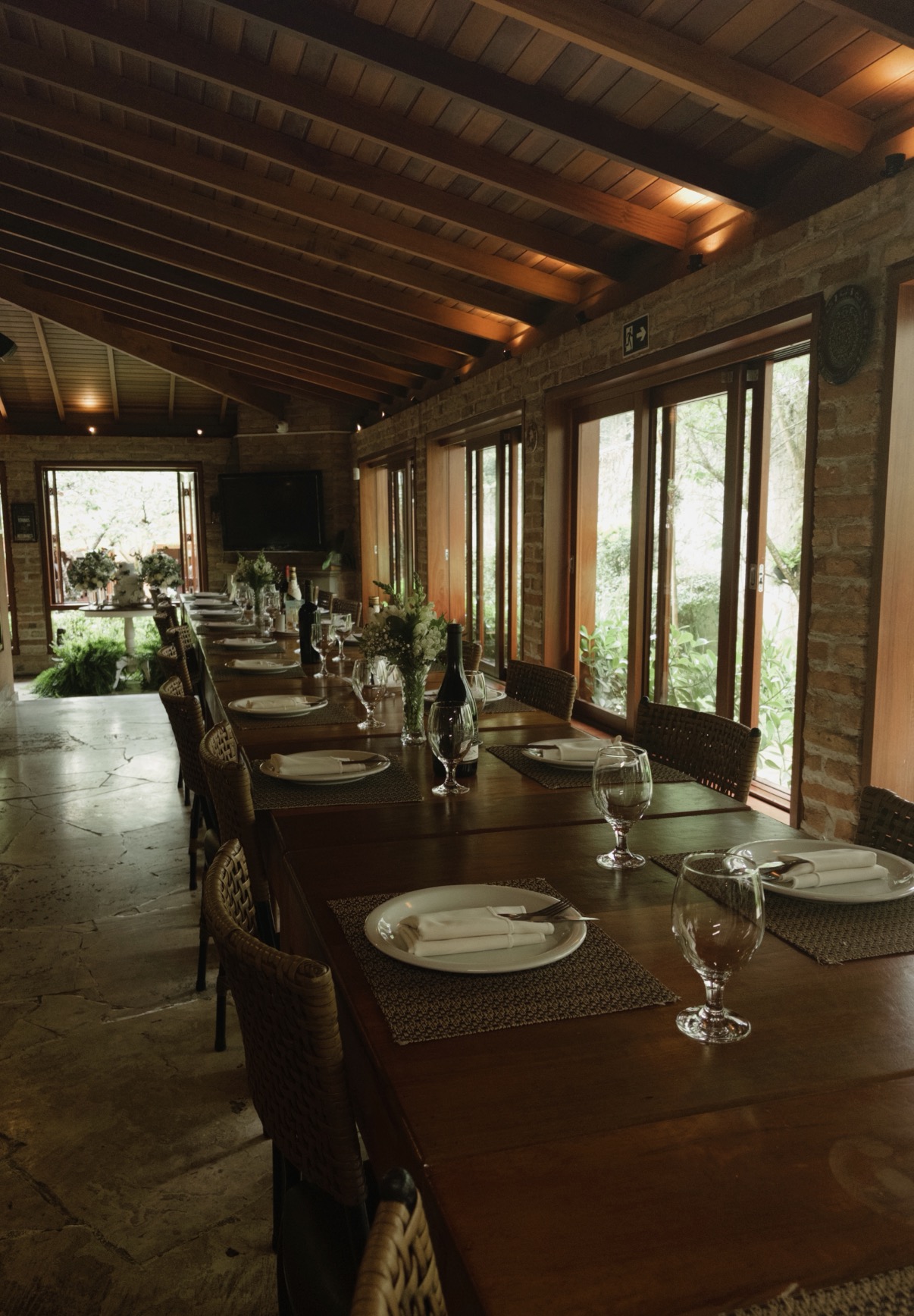 Salão de eventos do La Bastos com mesa longa, tijolos aparentes e vista para o jardim